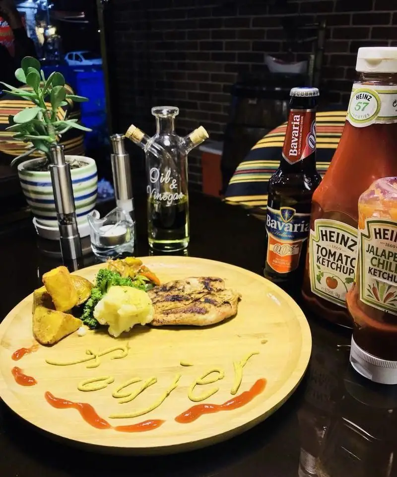 غذای خوشمزه کافه رستوران فوژر: جوجه گریل با سیب زمینی و سبزیجات، سرو شده با کچاپ، خردل و نوشیدنی باواریا در محیطی دلنشین و دنج.