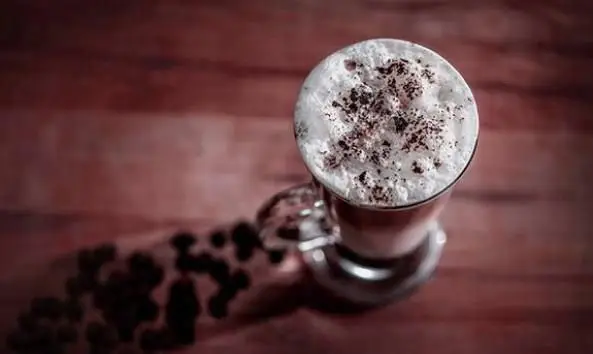 کاپوچینو داغ و خوشمزه کافی شاپ جحینا با کف شیر و پودر شکلات روی میزی چوبی و دانه های قهوه، تجربه‌ای دلنشین.