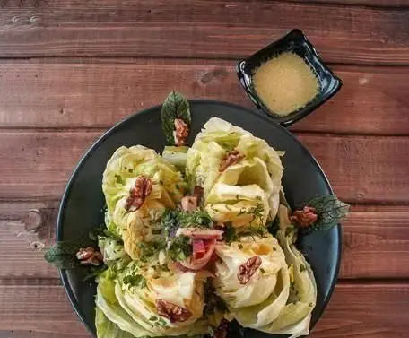 نمایی نزدیک از سالاد آیسبرگ لذیذ کافه ایوان با گردو و سبزیجات تازه، سرو شده با سس مخصوص در پس‌زمینه چوبی.