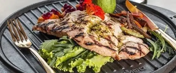 یک بشقاب زیبای مرغ گریل شده با سس پستو، سبزیجات رژیمی و سالاد تازه در کافی شاپ ایوان، مناسب برای یک وعده غذایی سالم و دلنشین.