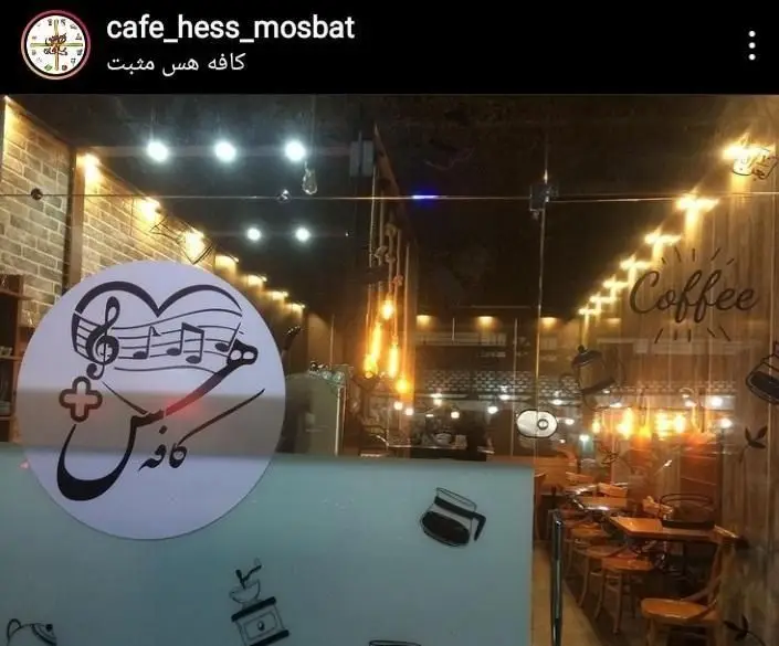 فضای داخلی کافه هس مثبت با دکوراسیون گرم و دلنشین، میز و صندلی چوبی، نورپردازی زیبا و لوگوی جذاب هس کافه روی شیشه.