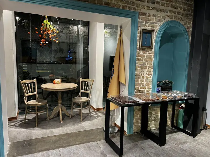 فضای داخلی گرم و صمیمی چوکوچاملی، شامل میز و صندلی چوبی و ویترین جذاب شکلات و دسرها، مناسب قرارهای دلنشین.