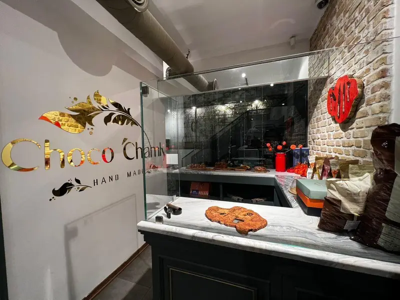 فضای داخلی لوکس فروشگاه شکلات دست‌ساز چوکوچاملی، نمایشگر محصولات مرغوب و دکوراسیون جذاب با لوگوی طلایی روی دیوار.