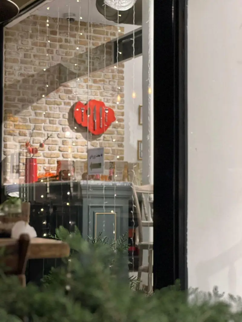 دکوراسیون داخلی گرم و دنج کافه چوکوچاملی با دیوار آجری، چراغ‌های زینتی و آویز ظروف آشپزخانه، فضایی دلنشین.