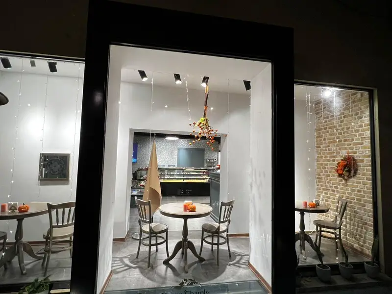 تصویری از ویترین و فضای داخلی کافه شیرینی و دسر چوکوچاملی با دکوراسیون پاییزی، میز و صندلی و نورپردازی دلنشین.