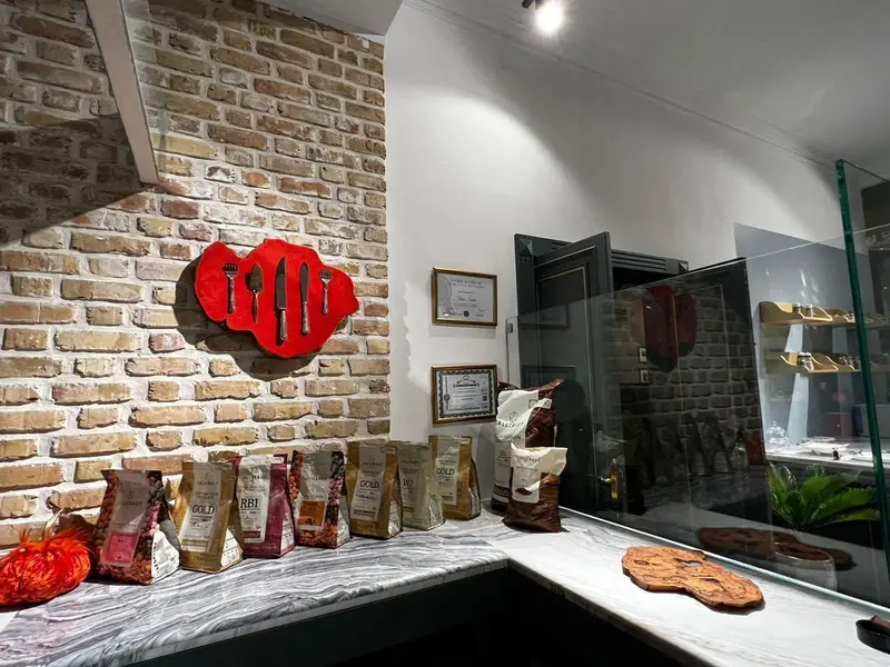 فضای داخلی دنج فروشگاه چوکوچاملی با دیوار آجری، دکور هنری چنگال و چاقو، گواهی ها، و محصولات قهوه/شکلات روی پیشخوان.