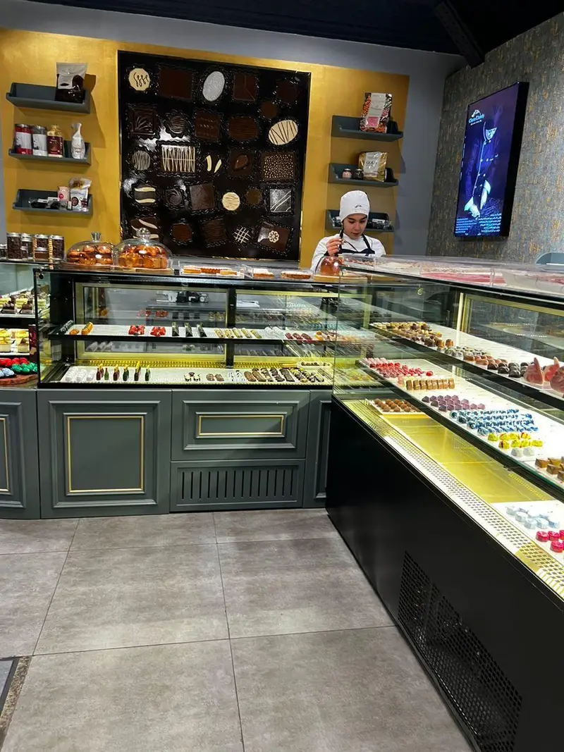 تصویری از داخل قنادی چوکوچاملی با ویترین‌های پر از شکلات‌های رنگارنگ، دسرها و شیرینی‌های تازه، آماده توسط سرآشپز.