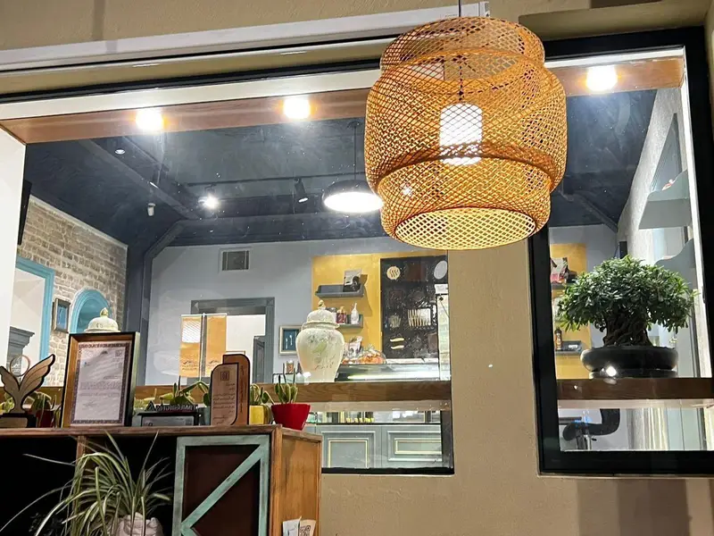 فضای داخلی دلنشین و دنج کافه چوکوچاملی، با لوستر حصیری چوبی، گیاهان سبز، درختچه بونسای و دکوراسیون چشم‌نواز در پشت شیشه.