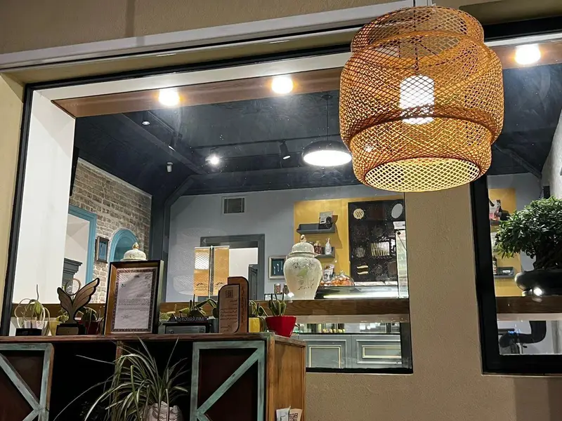 تصویری جذاب از دکوراسیون داخلی کافه چوکوچاملی با لوستر حصیری شیک، فضای گرم و دلنشین، پیشخوان پر از دسرها و گیاهان تزئینی.