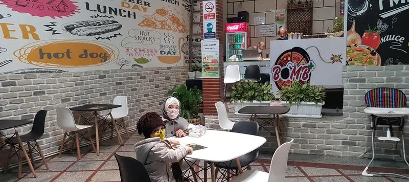 فضای داخلی پیتزا بمب پلاس، رستوران فست فود با دیوارنگاره‌های جذاب غذا، میز و صندلی مدرن و مشتریان از جمله کودکان.