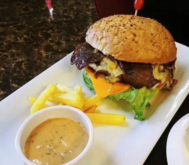 تصویری از همبرگر مخصوص با پنیر ذوب شده و کاهو، در کنار سیب‌زمینی سرخ‌کرده و سس، از منوی کافی‌شاپ ساقدوش.