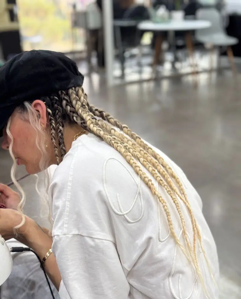 زنی با موهای بافته بلوند، کلاه مشکی و استایلی شیک در کافه وو، لذت بردن از فضای داخلی آرام و دلنشین.