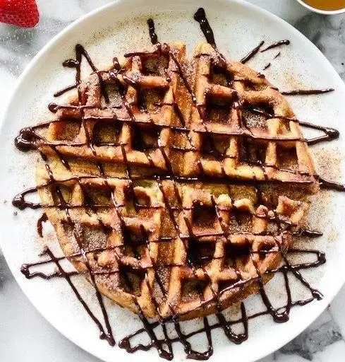 وافل طلایی و خوشمزه کافه وو با تزئین سس شکلات تلخ و پودر قند، انتخابی عالی برای یک صبحانه یا دسر فراموش‌نشدنی در کافه وو