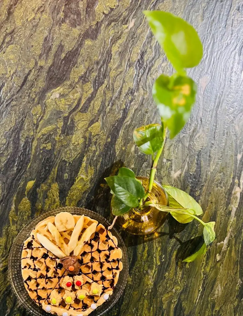 وافل مخصوص کافه وو با تکه‌های موز تازه، سس شکلات غلیظ و آبنبات‌های رنگارنگ. دسر خوشمزه برای تجربه ای شیرین در کافه وو.