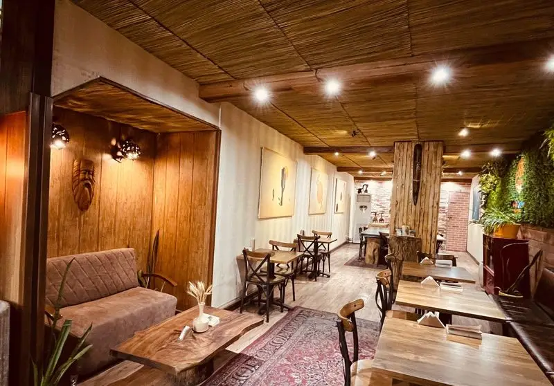نمای داخلی زیبای کافه وو با دکوراسیون گرم چوبی، میز و صندلی‌های روستیک، یک مبل راحتی و دیوارپوش گیاهی سبز دلپذیر.