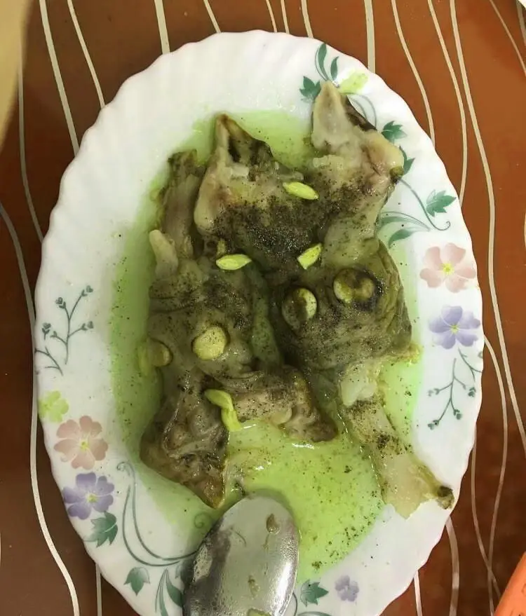 طباخی بره ناقلا: یک پرس کله پاچه سنتی و لذیذ، با آبگوشت سبز و چاشنی فلفل سیاه و سیر، آماده سرو برای مشتریان.