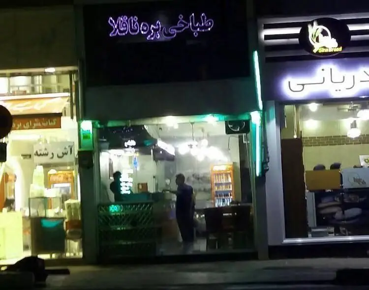 تصویر شبانه از نمای بیرونی "طباخی بره ناقلا" با تابلوی نئون روشن، ارائه دهنده غذاهای سنتی ایرانی از جمله کله پاچه و آش رشته.