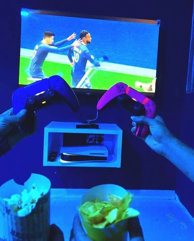 بازی دوستانه و پرشور فیفا با پلی استیشن 5 در محیط جذاب کافه گیم اسپارت، همراه با کنترلرهای دوال سنس و لذت خوراکی‌ها.