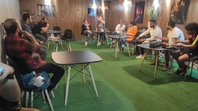 تصویری از دورهمی دوستانه و پرشور افراد در کافه گیم اسپارت، با فضای داخلی مدرن، میز و صندلی‌های شیک و کفپوش سبز چمن‌مانند.