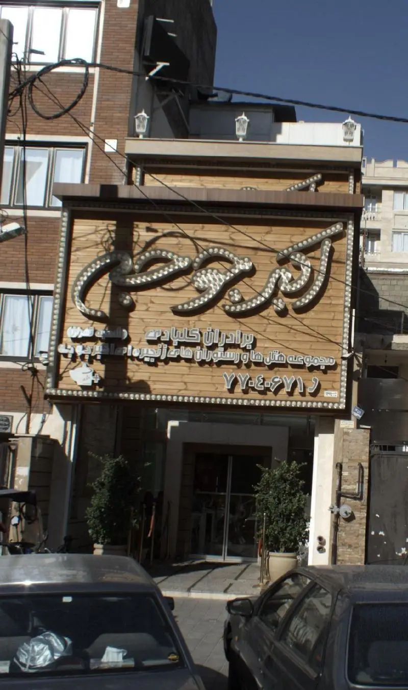 تصویر نمای رستوران زنجیره‌ای اکبرجوجه برادران کلبادی با تابلوی اصلی روشن، ورودی شیشه‌ای و شماره تلفن ٧٧٠٤٠٦٧١