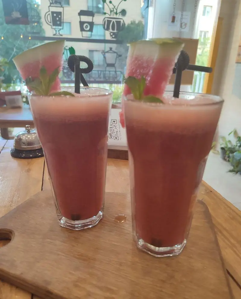 نوشیدنی‌های تابستانی کافه نار: دو لیوان اسموتی هندوانه خنک با برش‌های تازه هندوانه و نعنا روی تخته چوبی.