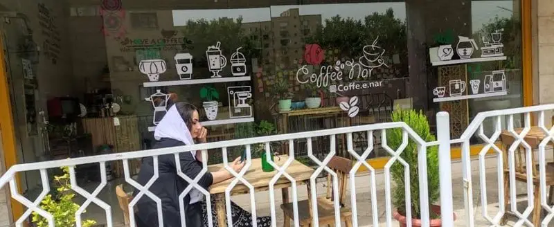 کافه نار، یک کافی شاپ با نمای شیشه ای و دکوراسیون طرح دار وسایل قهوه. مشتری در فضای باز دلنشین نشسته و از لحظات آرام لذت می برد.