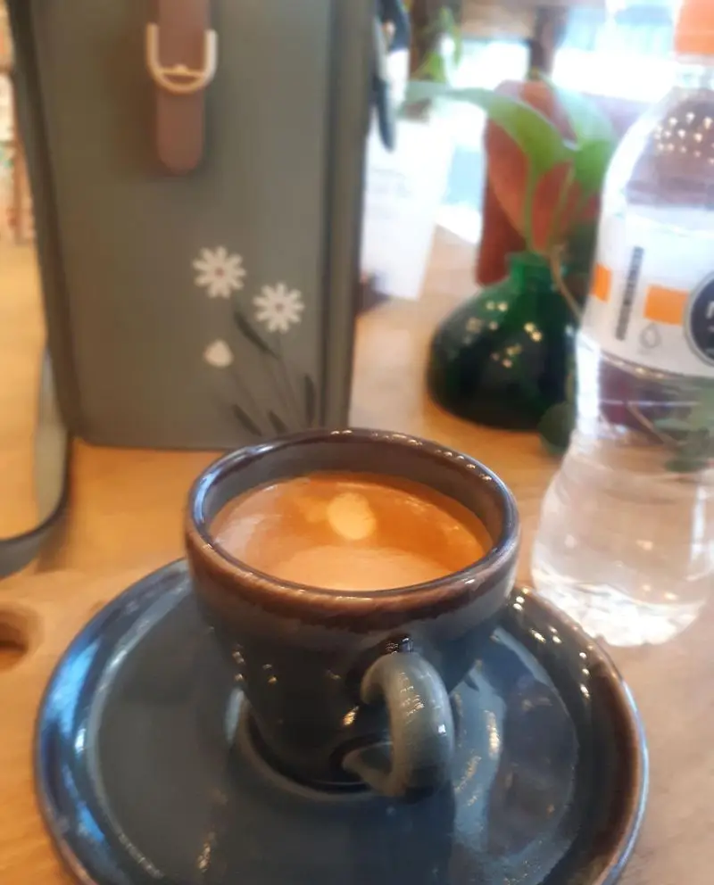 لذت نوشیدن قهوه اسپرسو تازه و با کیفیت در کافه نار، همراه با بطری آب و فضای دنج و دلپذیر این کافه.