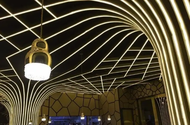 طراحی داخلی منحصر به فرد رستوران اکسون با سقف مدرن و نورپردازی خطی و منحنی. لوستر آویز طلایی و دیوارهای دکوراتیو فضای شیک و خاصی ایجاد کرده‌اند.