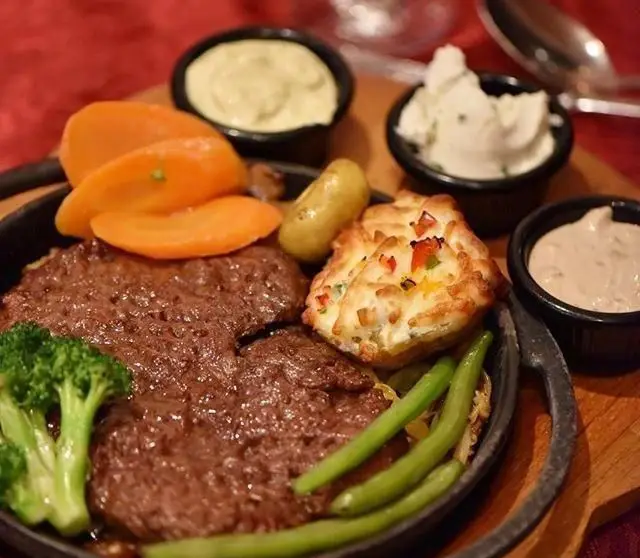 غذای لذیذ رستوران طهران پاریس: استیک در بشقاب داغ همراه با سبزیجات تازه (بروکلی، هویج، لوبیا سبز)، سیب‌زمینی و سس‌های متنوع.