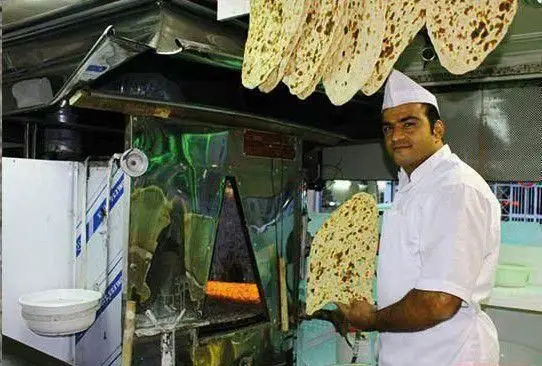 نانوای طباخی راک با لبخند، نان سنتی تازه را از تنور بیرون می‌آورد. نان‌های داغ و خوش‌رنگ برای مشتریان عزیز آماده می‌شوند.