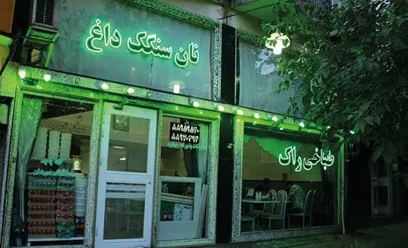 نمای بیرونی شبانه طباخی راک، رستورانی با نان سنگک داغ و غذاهای سنتی ایرانی با نورپردازی نئون سبز