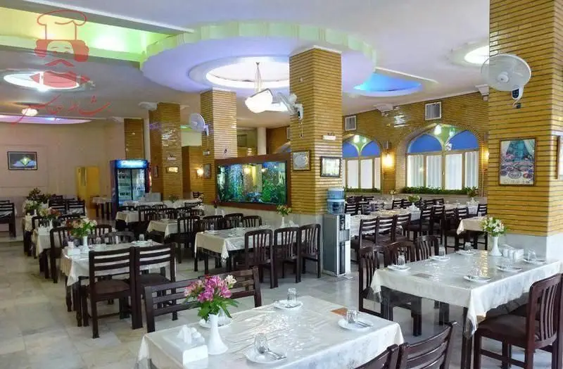 فضای داخلی دلباز و زیبای رستوران شاطر عباس با میز و صندلی‌های چوبی، دکوراسیون گرم و آکواریوم بزرگ، آماده پذیرایی از مشتریان.