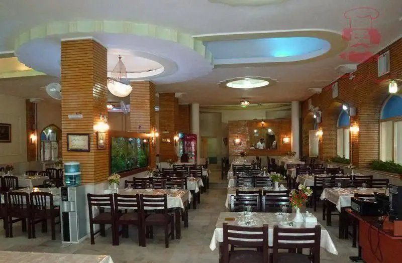فضای داخلی زیبای رستوران شاطر عباس با چیدمان مرتب میز و صندلی، دکوراسیون چوبی و آجری، آکواریوم بزرگ و نورپردازی دلنشین برای تجربه غذاخوری.