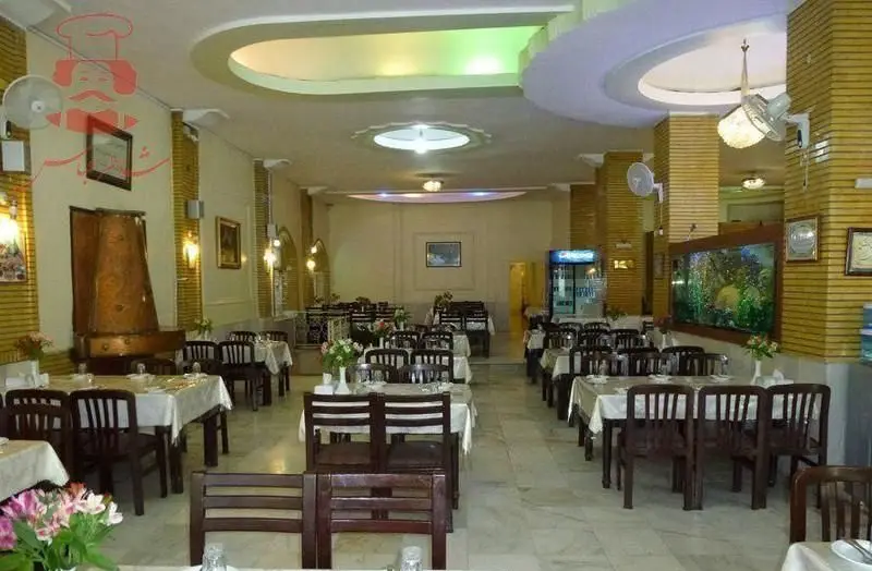 تصویر فضای داخلی وسیع رستوران شاطر عباس، با ردیف‌های میز و صندلی چوبی، دکوراسیون شیک، آکواریوم بزرگ و محیطی دلپذیر برای مشتریان.