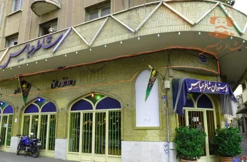 نمای بیرونی رستوران شاطر عباس، یک غذاخوری سنتی در ساختمانی آجری سبز رنگ با پنجره‌های قوسی آبی و یک موتور سیکلت در جلو.