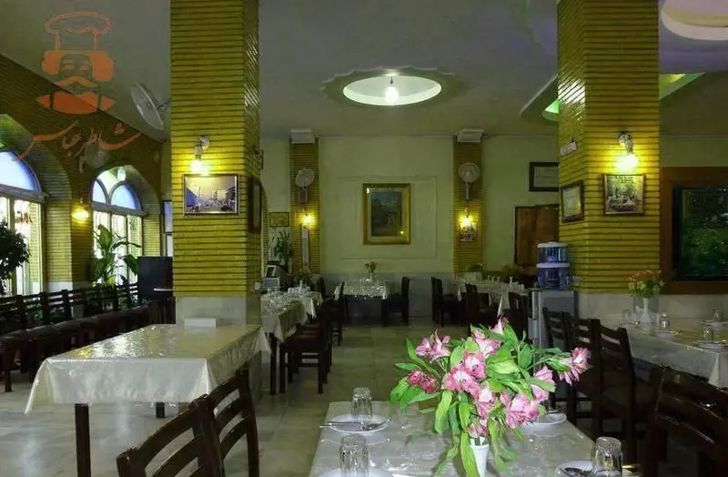 نمایی از سالن غذاخوری رستوران شاطر عباس با میزهای آماده، صندلی‌های چوبی، ستون‌های زرد و پنجره‌های بزرگ، فضایی آرامش‌بخش.