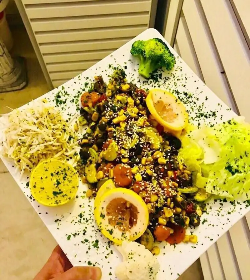 بشقاب غذای سالم رنگارنگ با ترکیب سبزیجات تازه، ذرت، بروکلی، جوانه، لیمو و کنجد در کافی شاپ ولو پارکو، انتخابی عالی برای گیاهخواران.