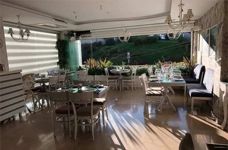 تصویری دلنشین از فضای داخلی روشن و شیک کافی شاپ ولو پارکو با میزهای آماده، دکوراسیون سفید و چشم‌انداز سبز دلنواز به بیرون.