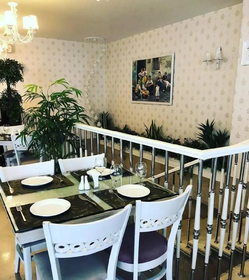 فضای داخلی دنج و شیک کافی شاپ ولو پارکو با میزهای آماده، صندلی‌های سفید، گیاهان سرسبز، نرده‌های مدرن و تابلوی هنری بر دیوار.