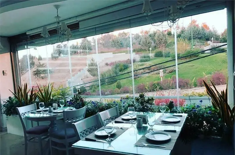 کافی شاپ ولو پارکو: نمایی دلنشین از فضای داخلی با میزهای چیده شده و منظره سبز پارک از پنجره‌های شیشه‌ای، ایده‌آل برای آرامش.