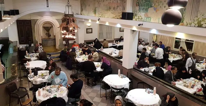 فضای داخلی وسیع و دلنشین رستوران هانی با مشتریان متعدد، دکوراسیون سنتی، آبنما و دیوارنگاره‌های زیبا، مناسب برای دورهمی خانوادگی.