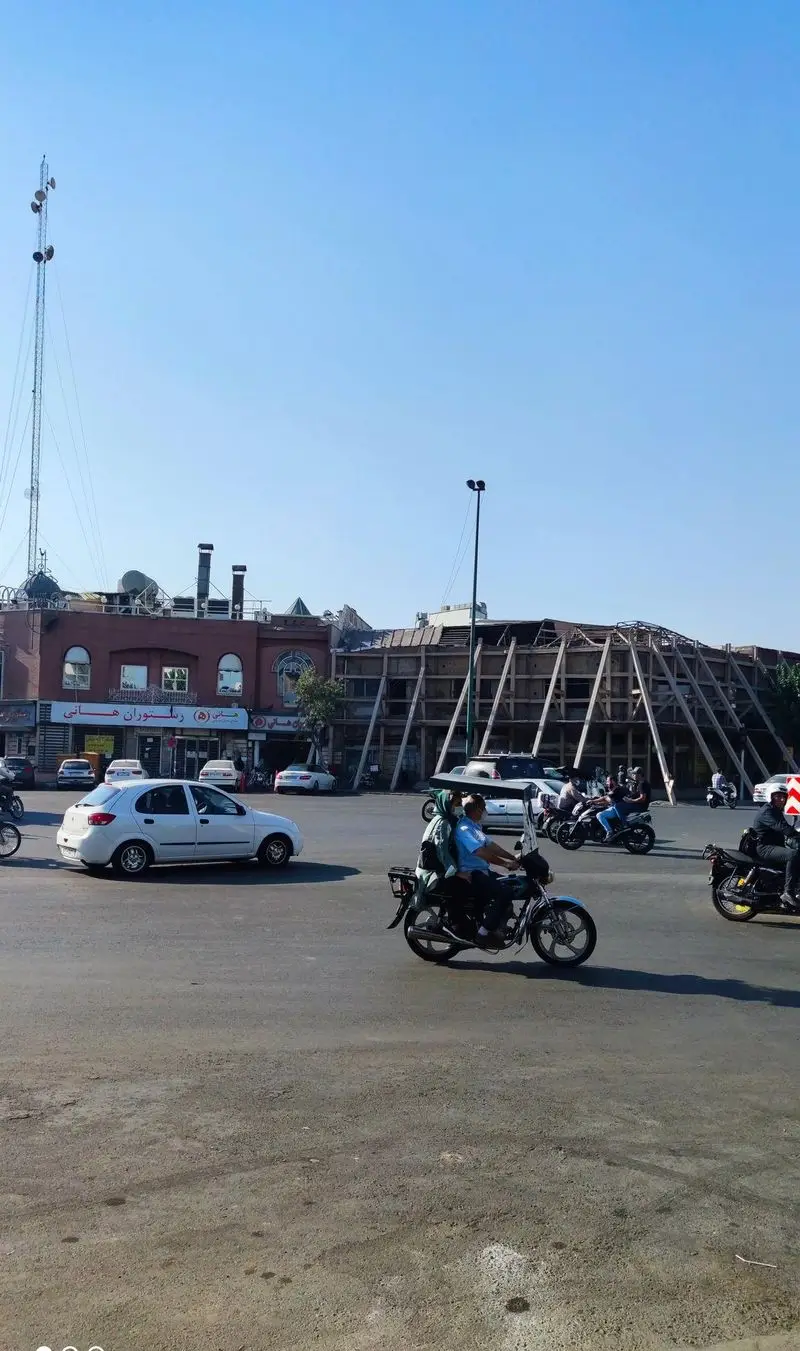 رستوران هانی با نمای آجری در کنار خیابانی شلوغ. تردد خودروها و موتورسیکلت‌ها زیر آسمان صاف آبی و برج مخابراتی.