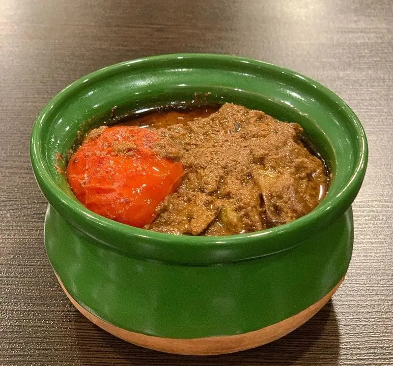 غذای سنتی و لذیذ رستوران هانی: خورشتی پرملات با تکه های گوشت، گوجه فرنگی و ادویه‌های معطر، سرو شده در کاسه سفالی سبز رنگ و زیبا.