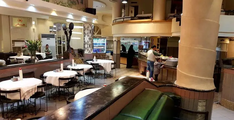 فضای داخلی دلنشین و شلوغ رستوران هانی، شامل میز و صندلی‌های چیده‌شده، کارکنان و مشتریان در بخش غذا و سالن اصلی.