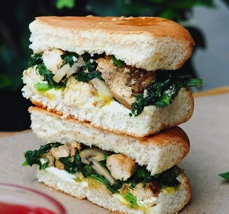 ساندویچ مرغ، اسفناج و قارچ رستوران برادران، برش خورده و لایه لایه، با نان تازه، سس و پنیر. یک غذای لذیذ و سالم.