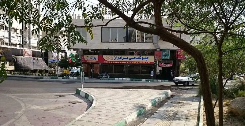 رستوران چلوکبابی برادران: نمای بیرونی ساختمان در خیابان با تابلوی مشخص، درختان و فضای سبز اطراف، آماده پذیرایی از مشتریان.