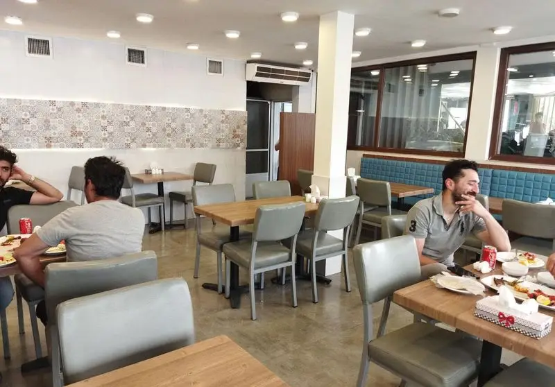 نمایی از رستوران برادران با فضای داخلی روشن و دلباز، شامل میزهای چوبی و صندلی‌های خاکستری رنگ و مشتریان در حال صرف غذا.