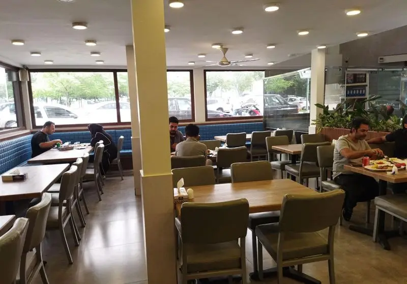 رستوران برادران، فضایی راحت و روشن برای صرف غذا با دوستان و خانواده، شامل میزهای چوبی، صندلی‌های مدرن و نیمکت‌های آبی کنار پنجره‌ها.