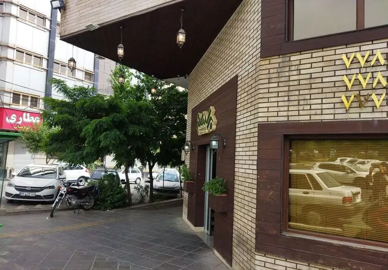 نمای خارجی رستوران برادران: ساختمانی با دیوارهای آجری و پانل‌های چوبی، ورودی با آرم و چراغ‌های آویز، همراه با درختان و خودروها در خیابان.