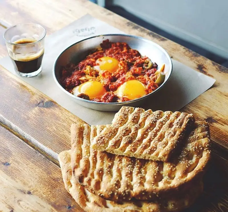 لذت صبحانه کامل در رستوران برادران: شاکشوکای داغ، نان بربری کنجدی و قهوه، تجربه‌ای دلنشین روی میز چوبی.